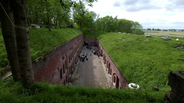 Cour intérieure du Fort de Seclin entourée de bâtiments en brique rouge, animée par des visiteurs, avec les remparts herbeux en surplomb.