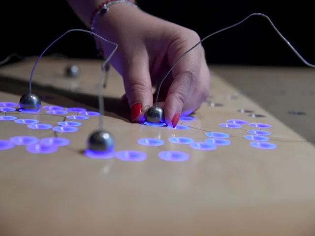 Main plaçant une bille métallique sur un plateau interactif lumineux au Forum départemental des sciences à Villeneuve-d’Ascq.