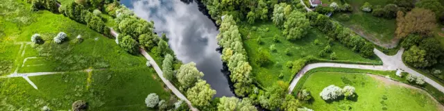 Vue aérienne du Lac du Héron entouré d’arbres et de sentiers, près de maisons rurales dans un paysage verdoyant.