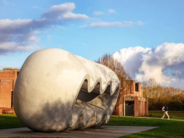 Grande sculpture blanche ondulée en plein air devant le musée LaM à Villeneuve-d’Ascq, sous un ciel bleu partiellement nuageux.