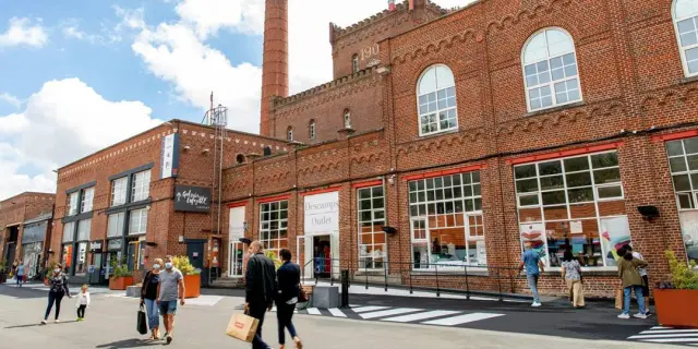 Façade en briques rouges de l’Usine à Roubaix, centre de marques installé dans une ancienne filature avec cheminée d’usine et passants en promenade.
