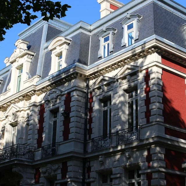 Façade de l’hôtel de ville de Croix, en briques rouges et pierre blanche, avec balcons en fer forgé et toit mansardé sous un ciel bleu.